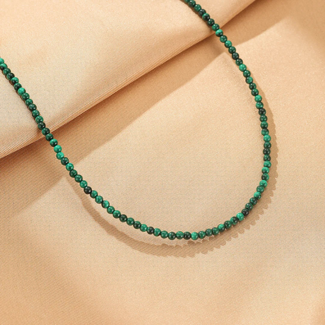 Collier "Harmonie Naturelle" en argent sterling avec de fines perles de malachite verte, posé sur un tissu beige satiné.