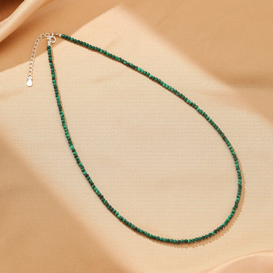 Collier "Harmonie Naturelle" en argent avec de fines perles de malachite verte, sur un fond beige satiné.