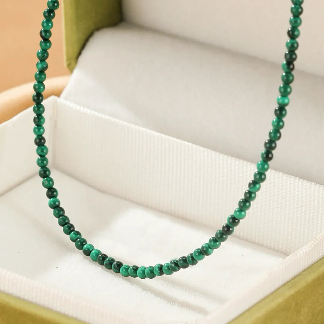 Gros plan d'un collier "Harmonie Naturelle" en malachite verte et argent, présentant de petites perles rondes sur un fond vert et blanc.