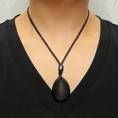 Collier "Profondeur Mystérieuse" avec un pendentif en obsidienne brute sur un cordon noir porté par une personne.