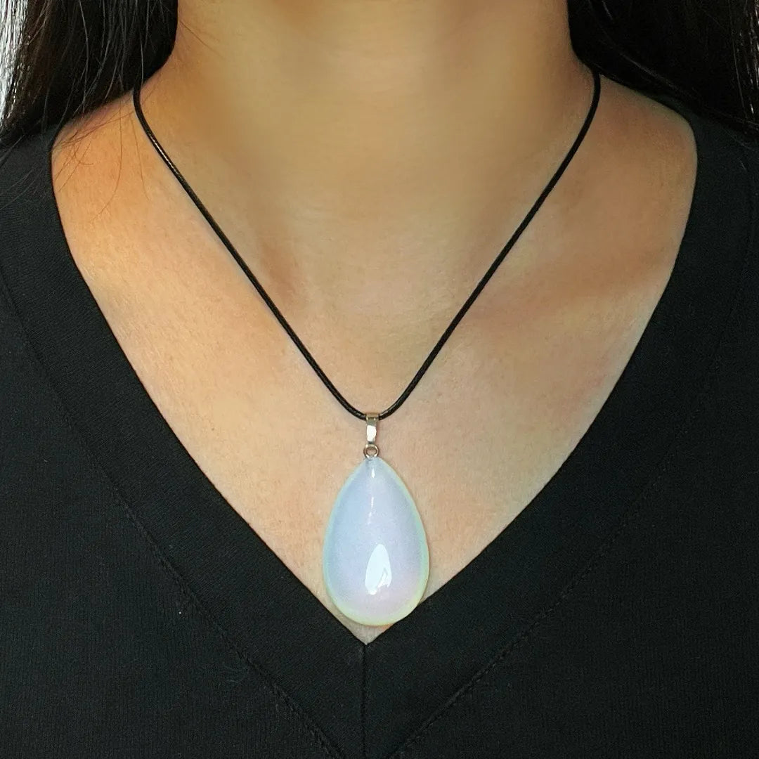 Gros plan sur un collier avec une opale blanche en forme de goutte sur un cordon noir porté par une personne vêtue d'un haut noir.