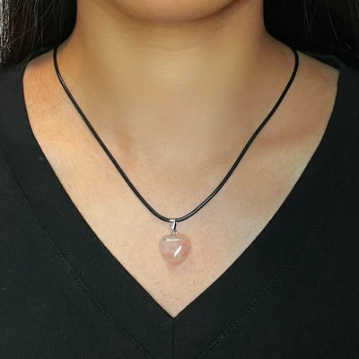 Collier avec un pendentif en forme de cœur en quartz rose sur un cordon noir porté par une femme.