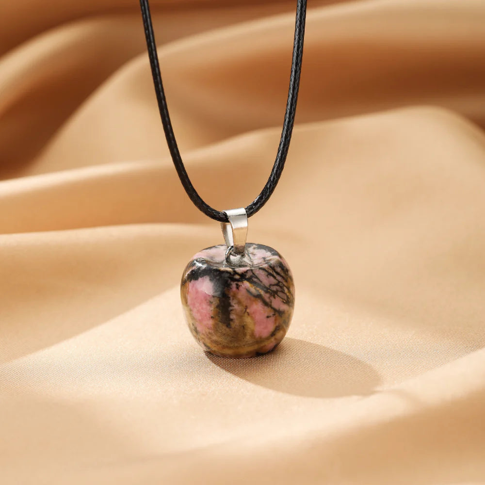 Collier avec un pendentif en forme de pomme en pierre de rhodonite rose et noire, monté sur un cordon noir.