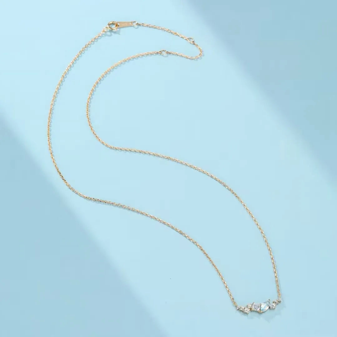 Collier avec trois pierres bleues claires et petites pierres blanches sur une chaîne dorée fine, sur fond bleu clair.