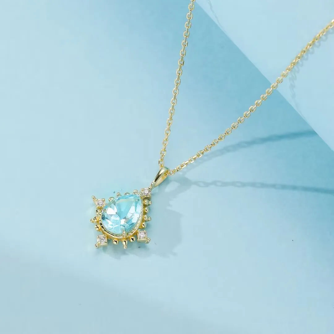 Collier Topaze "Rayons d'Élégance" en argent 925 avec pendentif goutte d'eau bleu clair entouré de petites pierres scintillantes.