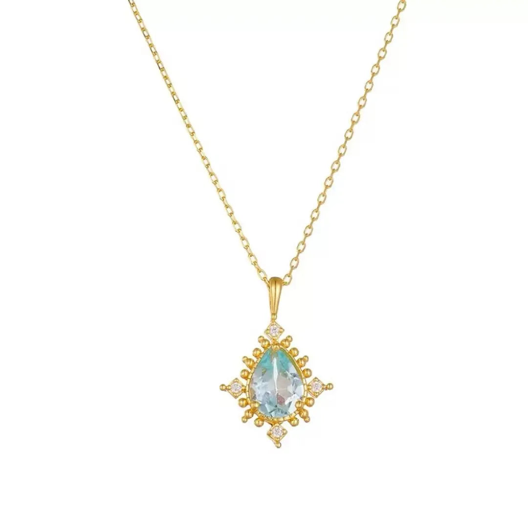 Collier avec un pendentif en forme de goutte d'eau bleu clair serti de diamants et entouré de petites perles dorées, sur une chaîne dorée.