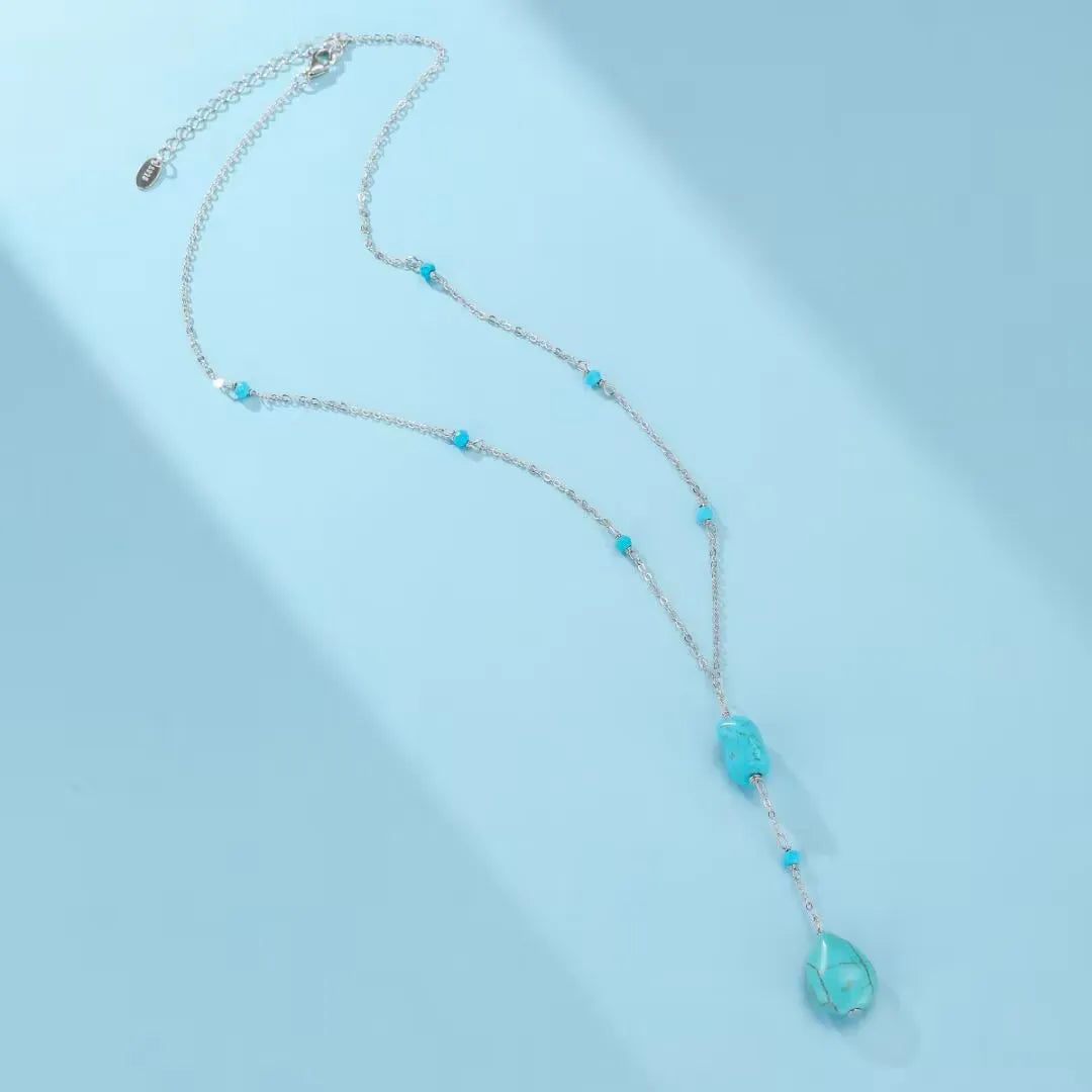 Collier "Voyage Céleste" en argent avec des pierres turquoise disposées le long de la chaîne et une pierre facettée en forme de goutte à l'extrémité.