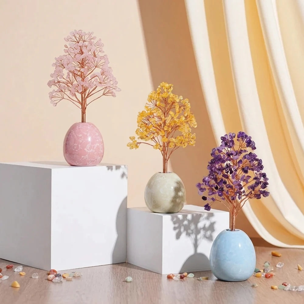 Arbre de Vie en pierres naturelles de couleur rose, jaune et violet, posé sur des socles blancs. L'arbre rose est dans un pot rose, l'arbre jaune dans un pot gris clair, et l'arbre violet dans un pot bleu clair.