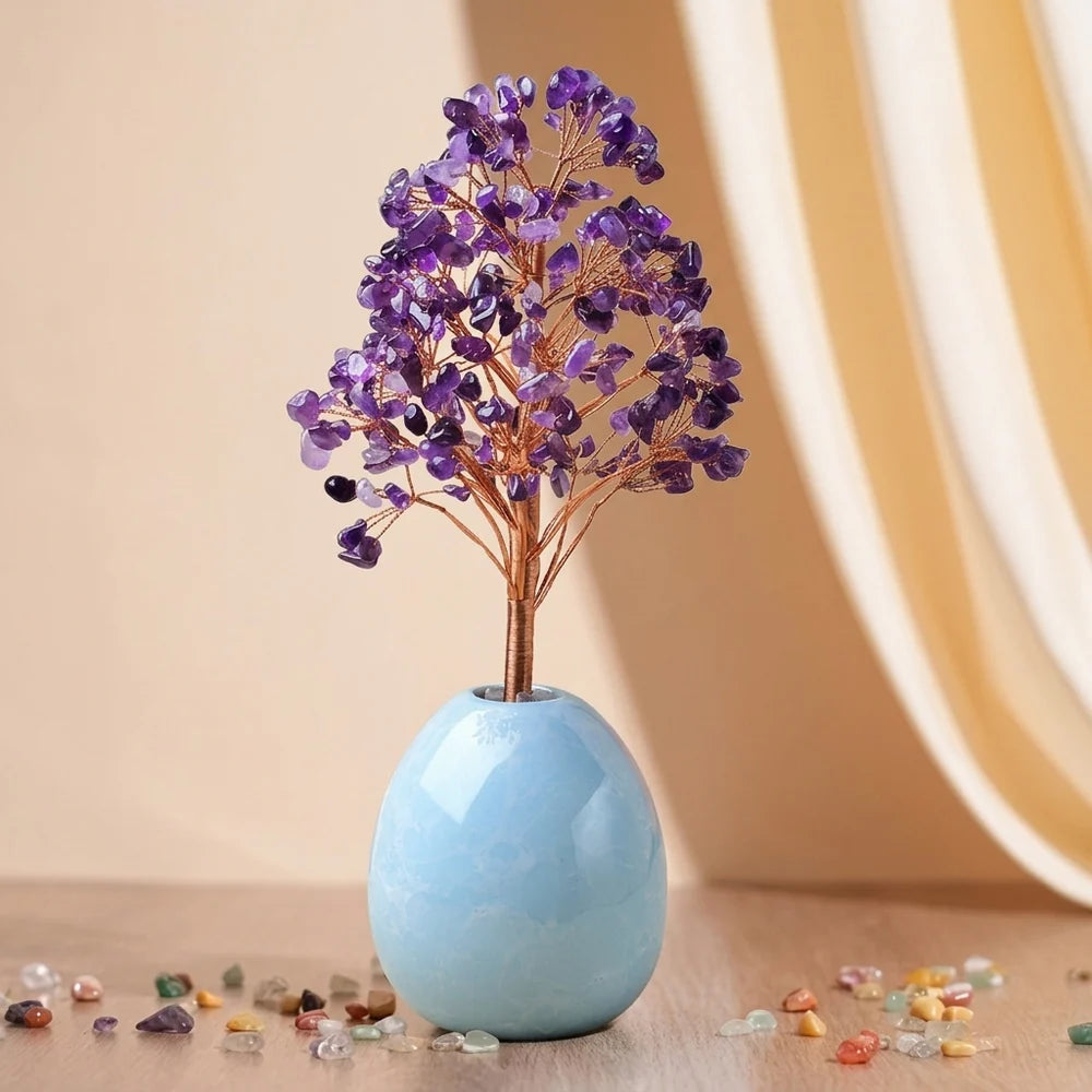 Arbre de Vie "Douce Harmonie" en améthyste avec des feuilles violettes et un tronc en fil de cuivre, posé dans un vase bleu clair en forme d'œuf. Des pierres colorées sont dispersées autour de la base.