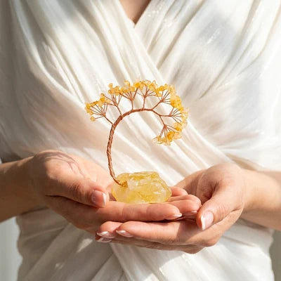 Arbre de vie décoratif en pierres naturelles de citrine monté sur un cristal brut de citrine, tenu dans des mains.