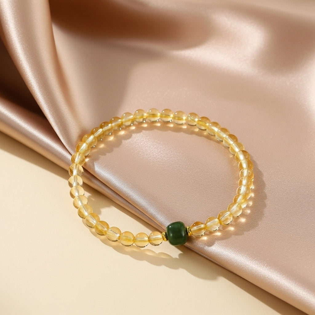 Bracelet en citrine avec une perle centrale verte, sur un fond de soie satinée beige.