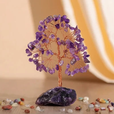 Arbre de Vie artisanal en pierres d'améthyste violettes, avec un tronc torsadé en fil de cuivre et une base en pierre d'améthyste brute, entouré de petites pierres décoratives.